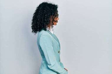 İş elbiseleri ve gözlük takan genç Latin kız, yan tarafa bakıyor, rahat poz veriyor, kendine güvenen bir gülümsemeyle doğal bir yüz ifadesi sergiliyor.. 