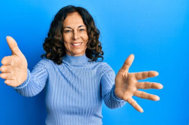 Orta yaşlı İspanyol kadın sıradan kıyafetler giyip kameraya bakıyor. Sarılmak için kollarını açmış gülümsüyor. Mutluluğu kucaklayan neşeli bir ifade.. 