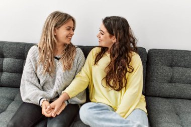 Mutlu gülümseyen ve el ele tutuşan genç çift evdeki kanepede oturuyor.