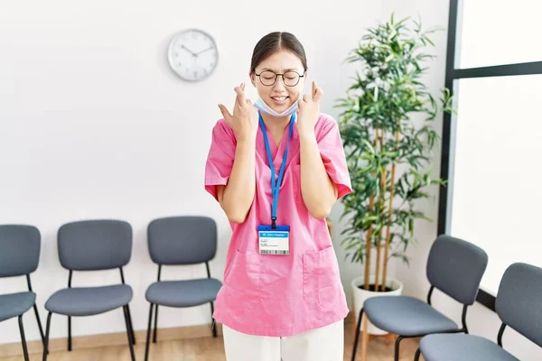 Young Asian Nurse Woman Medical Waiting Room Gesturing Finger Crossed — Stock Photo, Image