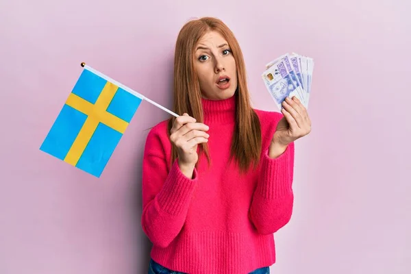 Young Irish Woman Holding Sweden Flag Krone Banknotes Shock Face — стоковое фото