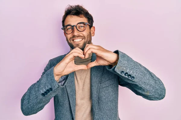 Sakallı, iş ceketli ve gözlüklü, aşıkken gülümseyen elleri ile kalp sembolü yapan yakışıklı bir adam. romantik kavram. 