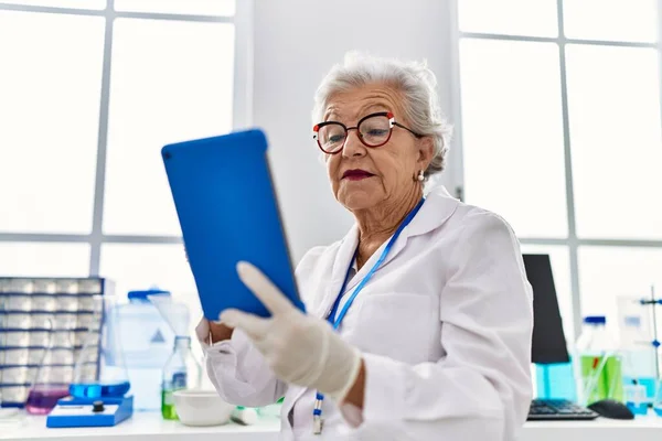 研究室でタッチパッドを使って科学者の制服を着たシニア白髪の女性 — ストック写真