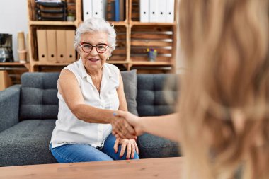 Psikoloji merkezinde kıdemli gri saçlı hasta ve psikoloji uzmanı el sıkışıyor.