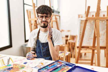 Sanat stüdyosunda sakallı bir İspanyol diş ağrısı ya da diş hastalığından dolayı acı dolu bir ifadeyle ağzına dokunuyor. dişçi 