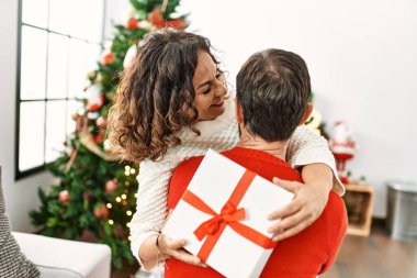 Orta yaşlı İspanyol çift mutlu bir şekilde gülümsüyor ve evde Noel hediyesi tutuyor..