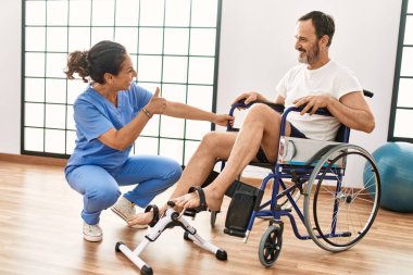 Orta yaşlı bir adam ve kadın fizik tedavi kliniğinde tekerlekli sandalyede pedal çeviriyorlar.