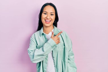 Güzel İspanyol bir kadın, burun piercingli, sıradan yeşil bir ceket giyiyor. Gülümsüyor, eli ve parmağı yana doğru uzanıyor. 