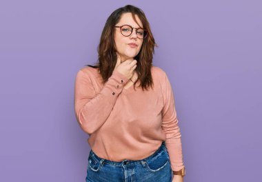 Genç ve cüsseli bir kadın günlük kıyafetler giyiyor ve gözlük takıyor. Ağrılı boynuna dokunuyor. Grip, mantar ve enfeksiyon yüzünden boğazı ağrıyor. 