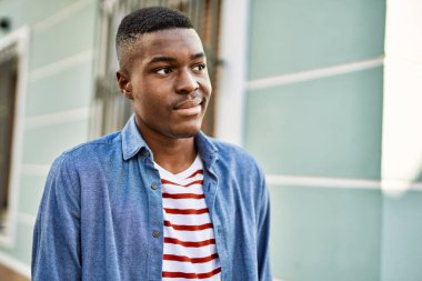 Genç Afrikalı Amerikalı adam gülümseyerek şehirde mutlu mesut duruyor..