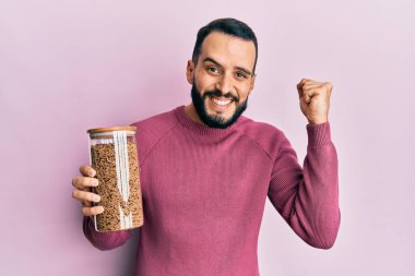 Sakallı genç adam elinde sağlıklı tahıl gevreği kavanozuyla gururla bağırıyor zaferi ve başarıyı kutluyor. 