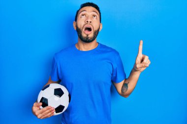 Futbol topunu tutan İspanyol sakallı adam şaşırmış ve şaşırmış bir şekilde yukarı baktı ve parmaklarıyla işaret etti ve kolunu kaldırdı.. 