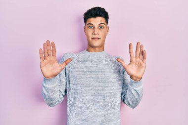 Günlük giysiler giyen genç İspanyol adam korku ifadesinden korkuyor ve dehşete düşüyor. El hareketlerini durdur, şok içinde bağır. panik konsepti. 