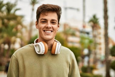 Şehirde kulaklık takarak mutlu gülümseyen genç İspanyol adam..