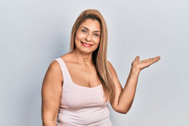 Orta yaşlı İspanyol kadın kolsuz tişörtlü, sıradan giyinmiş neşeli bir şekilde gülümseyen ve avuç içi kameraya bakan.. 