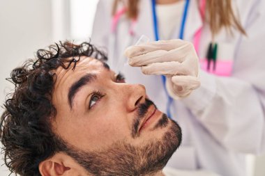 Doktor üniforması giyen kadın ve erkek kliniğe göz damlası damlatıyor.