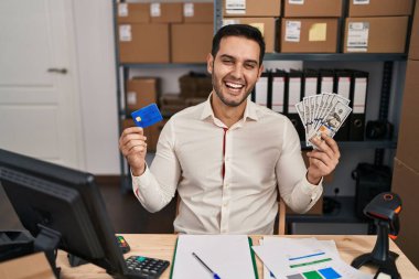 Sakallı genç İspanyol bir adam küçük işletmelerde çalışıyor. Elinde banknotlar ve kredi kartları var. Gülmekten kırılıyor ve kahkahalar atıyor.. 