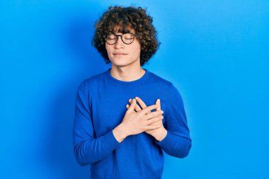 Yakışıklı, sıradan kıyafetler ve gözlük takan, elleri göğsünde, gözleri kapalı gülümseyen ve yüzünde minnet ifadesi olan bir genç. sağlık kavramı. 