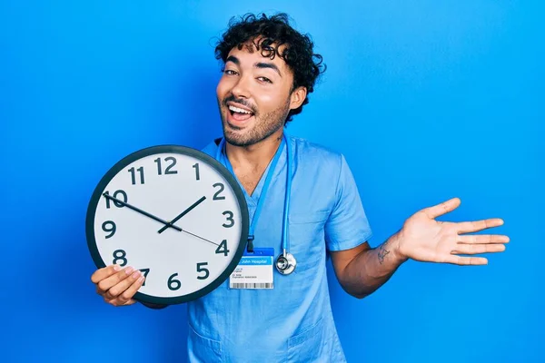 Joven Hombre Hispano Vistiendo Uniforme Enfermero Azul Sosteniendo Reloj Celebrando —  Fotos de Stock