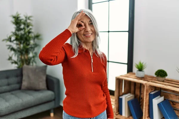 stock image Middle age grey-haired woman wearing casual clothes standing at home smiling happy doing ok sign with hand on eye looking through fingers 