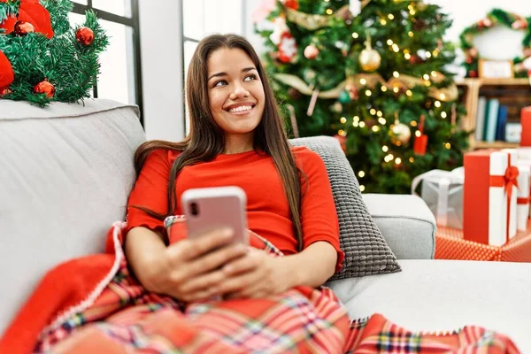 Νεαρή Λατίνα Γυναίκα Που Χρησιμοποιεί Smartphone Κάθεται Από Χριστουγεννιάτικο Δέντρο — Φωτογραφία Αρχείου
