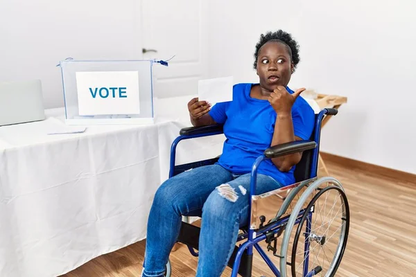 Młoda Afrykanka Siedząca Wózku Inwalidzkim Głosująca Zaskoczenia Wskazując Palcem Bok — Zdjęcie stockowe