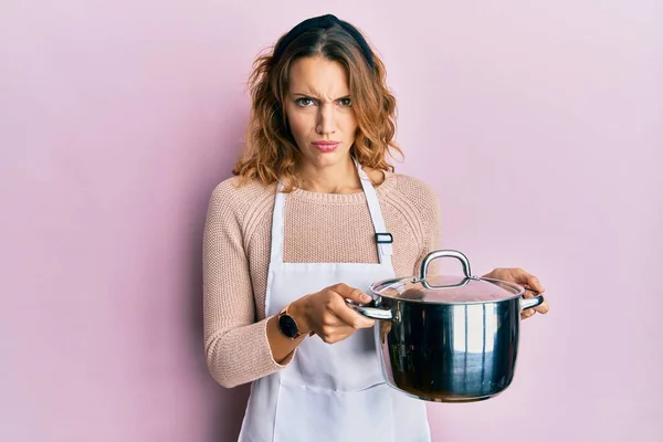 Mujer Caucásica Joven Usando Delantal Sosteniendo Olla Cocina Escéptica Nerviosa — Foto de Stock