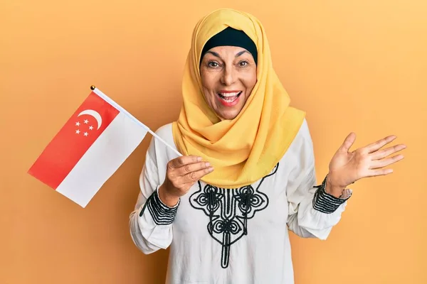 Średniowieczna Latynoska Kobieta Hidżabie Trzymająca Flagę Singapore Świętująca Osiągnięcie Szczęśliwym — Zdjęcie stockowe