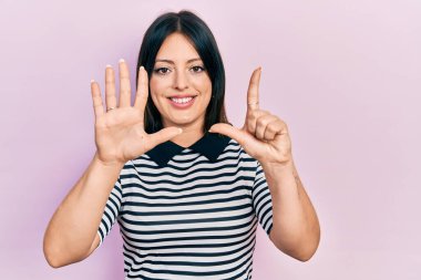 Genç İspanyol kadın gündelik kıyafetler giyer ve yedinci parmaklarını göstererek gülümseyerek mutlu ve kendinden emin bir şekilde gösterir.. 