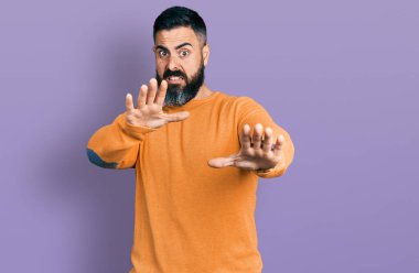 Sakallı, sıradan bir kazak giyen, korku ifadesinden korkan ve dehşete düşmüş İspanyol bir adam. El kol hareketi yapmayı kes, şok içinde bağır. panik konsepti. 