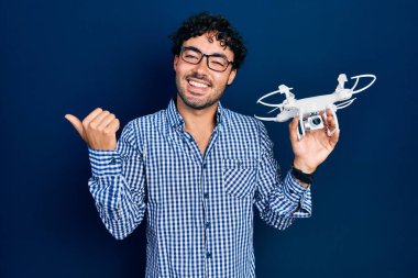Genç İspanyol bir adam İHA 'yı elinde tutuyor başparmağıyla yan tarafa bakıyor mutlu bir şekilde ağzı açık gülümsüyor. 