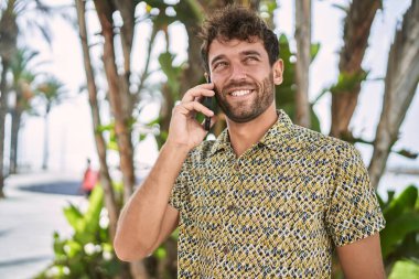 Genç İspanyol adam gülümsüyor. Parktaki akıllı telefondan konuşuyor.