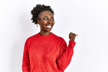 Genç Afro-Amerikalı kadın, izole edilmiş arka planda günlük giysiler giyip gülümsüyor, gülümsüyor ve başparmağıyla yüzünü yukarı kaldırıyor.. 