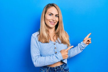 Gündelik kıyafetler giyen, gülümseyen ve kameraya bakan genç beyaz bir kadın iki elini ve parmağını yana doğru uzattı.. 