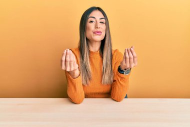 Latin kökenli genç bir kadın, gündelik giysiler içinde masada oturuyor. Elleriyle para hareketi yapıyor. Maaş ve milyonerlik işi istiyor. 