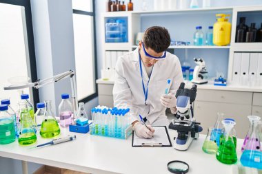 Laboratuvarda panoya yazı yazan, bilim adamı üniforması giyen İspanyol bir genç.