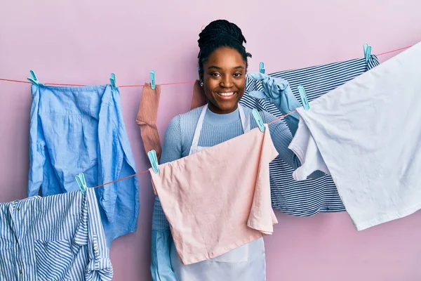 拥有辫子的非洲裔美国女人在晾衣绳边洗衣服 微笑着 自信地摆姿势 手拿着小尺寸的标志 手拿着手指 手拿着相机 计量概念 — 图库照片