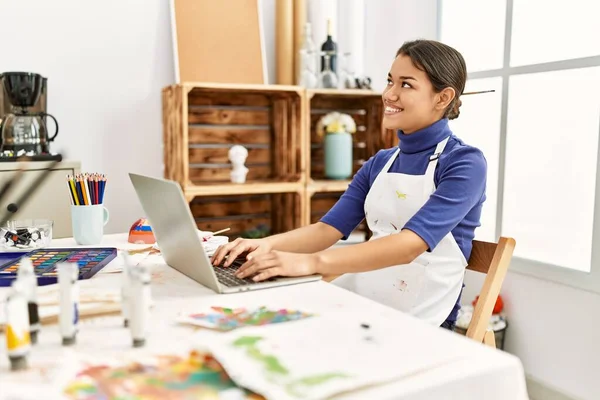 年轻的拉丁女人坐在艺术工作室的桌子上 用笔记本电脑 — 图库照片