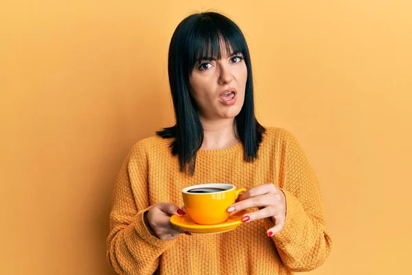 Jonge Spaanse Vrouw Houdt Koffie Shock Gezicht Zoek Sceptisch Sarcastisch — Stockfoto