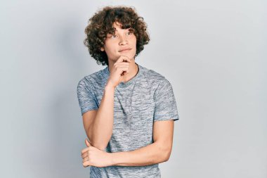 Gri bir tişört giyen yakışıklı genç adam kameraya kolları çapraz ve çenesi açık gülümsüyor. Olumlu düşünmek. 