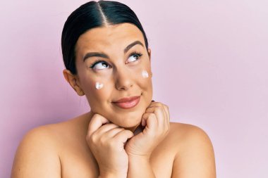 Güzel esmer kadın, üstsüz, yüz kremi sürmüş, gülümsüyor, yan tarafa bakıyor ve düşünüyor.. 