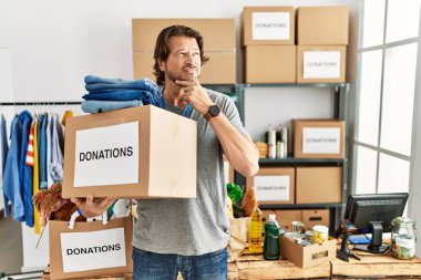 Gönüllü olarak bağış kutusunu tutan yakışıklı, orta yaşlı bir adam kameraya kollarını kavuşturup gülümseyen ve çenesini kaldıran birine bakıyor. Olumlu düşünmek. 