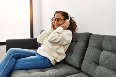 Orta yaşlı İspanyol kadın evde müzik dinlerken kendinden emin gülümsüyor.