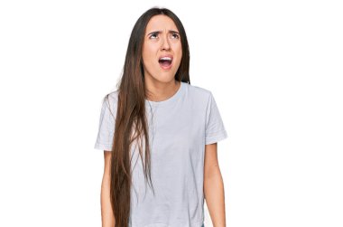 Latin asıllı genç bir kız, günlük beyaz tişört giyiyor kızgın ve kızgın bağırıyor, sinirden köpürüyor, öfkeyle bağırıyor. öfke ve agresif konsept. 