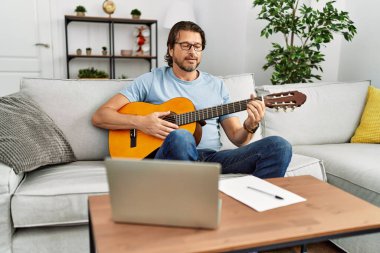 Orta yaşlı beyaz bir adam evde klasik gitar çalıyor.