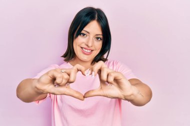 Gündelik pembe tişört giyen, aşık gülümseyen, elleriyle kalp sembolü yapan genç İspanyol kadın. romantik kavram. 