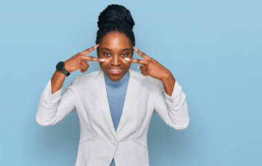 Genç Afro-Amerikan kadın iş kıyafetleri içinde barış sembolü yapıyor, parmaklarının üzerinde gülümseyerek zaferi gösteriyor. 