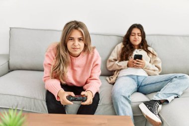 Kız video oyunu oynuyor ve kız arkadaşı evde akıllı telefon kullanıyor..