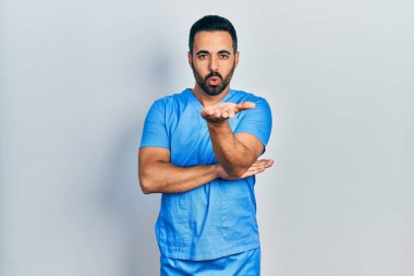 Yakışıklı, sakallı, mavi erkek hemşire üniforması giyen yakışıklı bir adam. Kameraya bakıyor ve havada öpüşüyor. Güzel ve seksi. aşk ifadesi. 