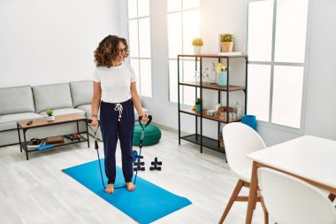 Olgun İspanyol kadın evdeki oturma odasında lastik bantlarla egzersiz yapıyor.